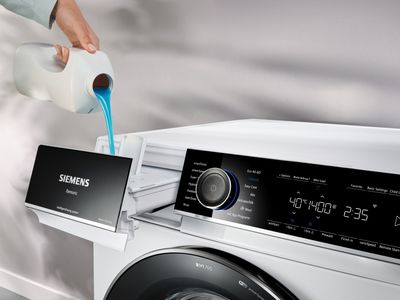 Une main de femme verse de la lessive dans le tiroir ouvert d'un lave-linge.