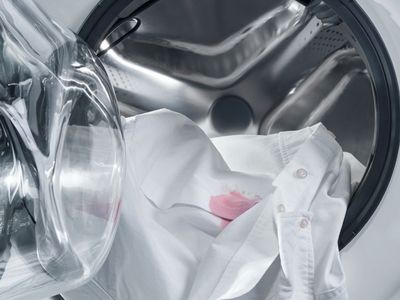Ein weisses Hemd mit einem roten Weinfleck wird in eine Waschmaschine gegeben.
