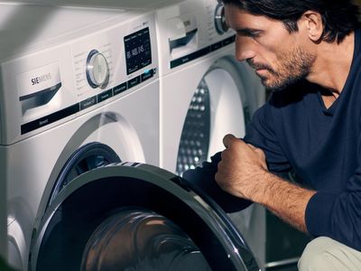 Nahaufnahme eines Mannes, der eine Waschmaschine belädt. Neben der Waschmaschine befindet sich ein Trockner.