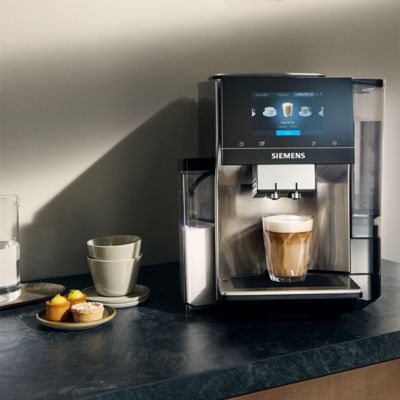 Une machine à café Siemens sur un comptoir avec un café sous le distributeur et des produits de boulangerie à côté.