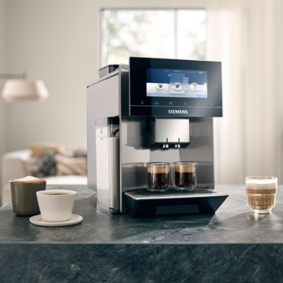 Une machine à café Siemens EQ900 plus au comptoir avec des expressos et d'autres cafés à côté.