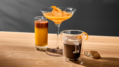 Trois verres de cocktails à base d'expresso présentés de manière créative sont posés sur un plan de travail en bois clair à côté d'un biscuit.