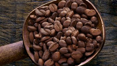Grains de café torréfiés dans une cuillère en bois  posée sur une surface en bois rustique.