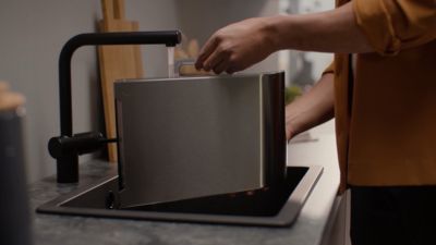 Iemand vult het waterreservoir van een Siemens koffiemachine onder de kraan.