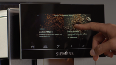 Un doigt touchant l'option baristaMode sur l'écran tactile d'une machine à café Siemens.