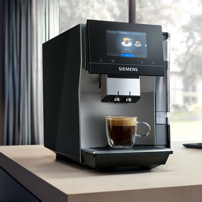 
         Ekspres EQ700 na jasnym drewnianym blacie z czarną kawą pod dozownikiem.
        