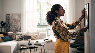 Une femme accroche un cadre au mur dans un salon moderne.