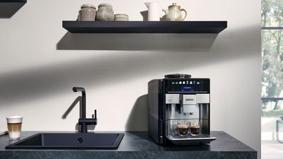 Une machine à café EQ700 sur un comptoir en marbre à côté d'un évier de cuisine et un latte macchiato.