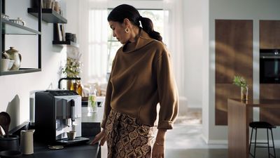 Une femme à côté d'une machine à café automatique EQ300 dans un salon moderne.