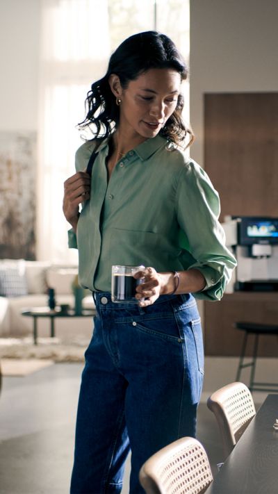 Een vrouw staat in een moderne woonkamer met een kop americano in haar linkerhand.