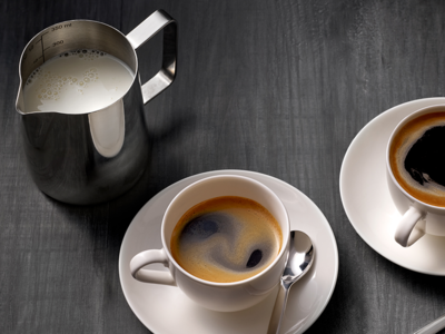 Bovenaanzicht van twee americano's en een kan melk op een donkere houten tafel.