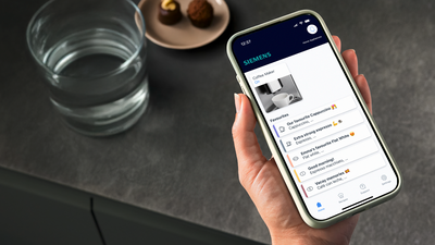 Une femme tenant un smartphone avec l'application Siemens Électroménager à l'écran.