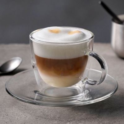 Gros plan d'un cappuccino dans une tasse en verre et une soucoupe sur un comptoir.