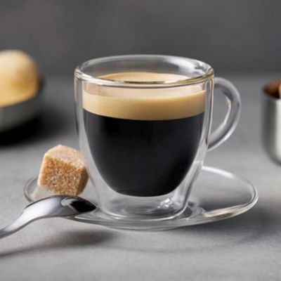 Une tasse d'expresso transparente avec sa soucoupe, une cuill&egrave;re &agrave; caf&eacute; et du sucre.