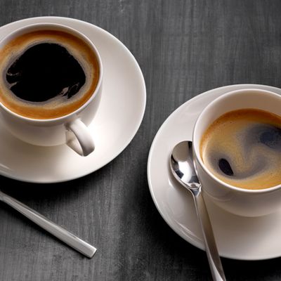 Un café americano dans une tasse en verre sur un comptoir en bois clair.