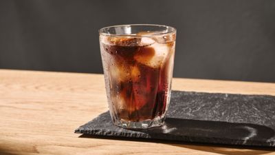 Verre transparent contenant du caf&eacute; avec des gla&ccedil;ons, pos&eacute; sur une surface en bois.