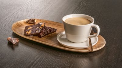 Une tasse de café et un morceau de chocolat sur un plateau en bois.