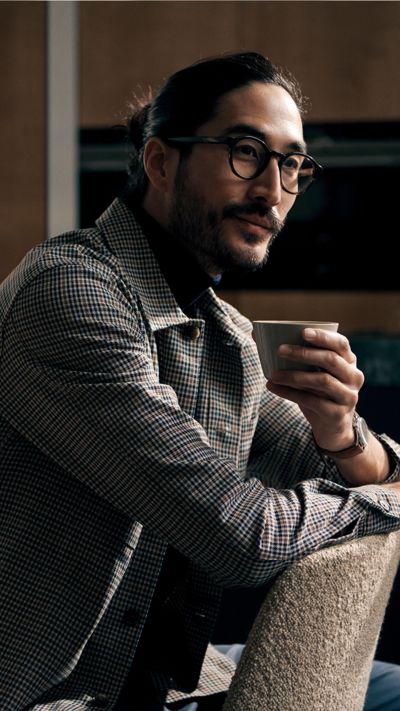 Un homme assis sur une chaise d&eacute;guste une tasse de th&eacute; dans une cuisine. En arri&egrave;re-plan, une machine &agrave; caf&eacute; Siemens est pos&eacute;e sur le plan de travail.