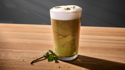 Un verre de matcha latte avec de la mousse de lait, pos&eacute; sur une surface en bois.