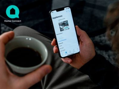 Een man houdt een smartphone vast met de Siemens Home Connect-app en in de andere hand een kop koffie.
