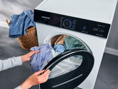 Person loading a Siemens washing machine with clothes.