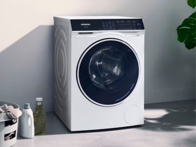 A Siemens front-load washing machine in a room with laundry accessories.