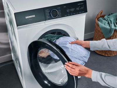 Person loading clothes into a Siemens washing machine.