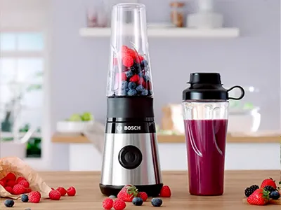 Bosch Miniblender VitaPower Serie 2 with red fruits and a smoothie-filled To-Go-bottle on a kitchen shelf.