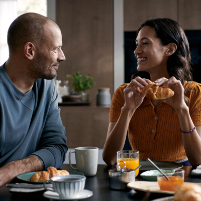 Una coppia felice fa colazione con dei croissant al tavolo della cucina.