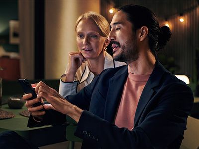 Ein Mann und eine Frau sitzen entspannt in stimmungsvoller Abendatmosphäre und betrachten gemeinsam etwas auf dem Smartphone