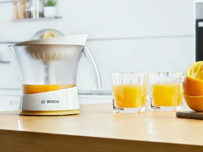 The Bosch citrus press VitaPress standing on a kitchen worktop with orange juice.
