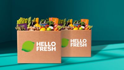 Zwei HelloFresh-Boxen mit frischem Gemüse, Obst & Mahlzeitensets vor blaugrünem Hintergrund.