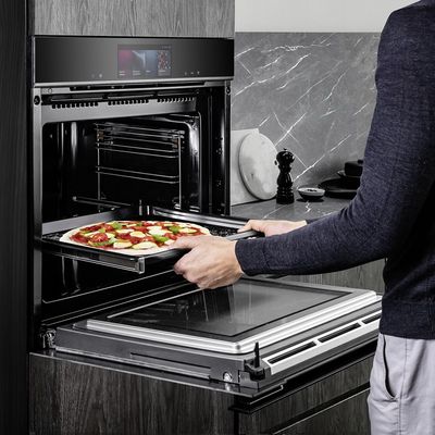 Un'immagine mostra un uomo che regge una teglia di pizza con entrambe le mani, pronto a inserirla in un forno da incasso Siemens iQ700.