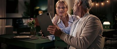 Paar zitten aan tafel, met behulp van digitale tablet, indoor avond setting met verlichting.