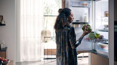 Vrouw in bloemen jurk staan voor open koelkast, houden verse producten. 