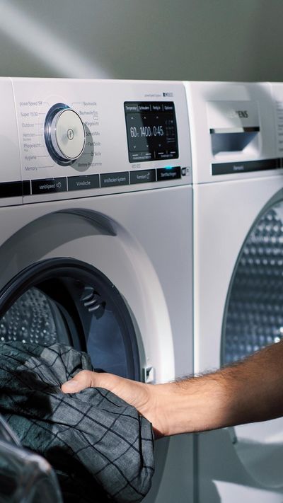 Una persona introduce una prenda en una lavadora Siemens