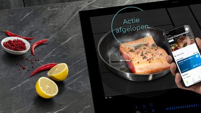 Sizzling visfilet in pan, gegarneerd met citroen plakjes en rode pepercorns, met smartphone tonen kookinstructies. 