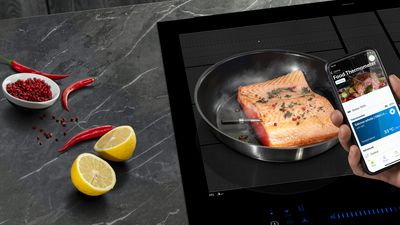 Sizzling visfilet in pan, gegarneerd met citroen plakjes en rode pepercorns, met smartphone tonen kookinstructies. 
