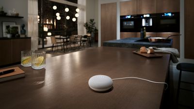 Keuken met slimme speaker op eiland, glazen, notitieblok en sfeervolle eetruimte op achtergrond. 