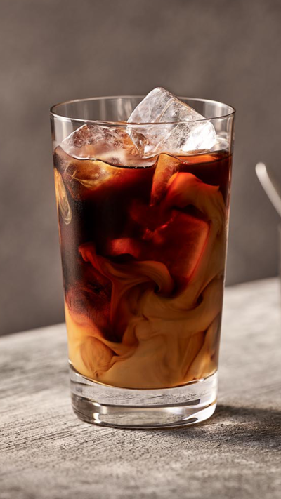 Verre de caf&eacute; glac&eacute; avec des gla&ccedil;ons pos&eacute; sur un plan de travail gris clair.