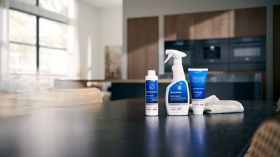 Imagem promocional com produtos de limpeza Siemens: spray, produto de limpeza de fornos, com um cenário de cozinha moderno.