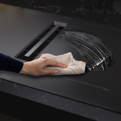 Een hand veegt de matte kookplaat schoon.