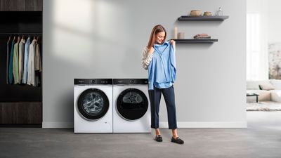 Uma pessoa segura uma camisa azul clara numa lavandaria moderna, equipada com máquina de lavar e secar roupa.