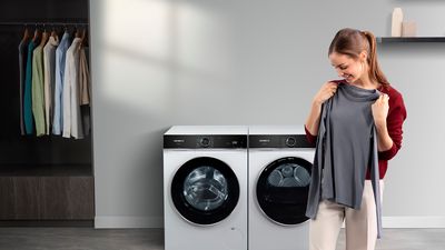 Uma mulher segura uma camisa cinzenta em frente a máquinas de lavar e secar roupa modernas da Siemens.