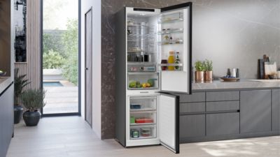 Keuken met zwarte koelkast, deur open, schappen vol groente, fruit en sauzen.