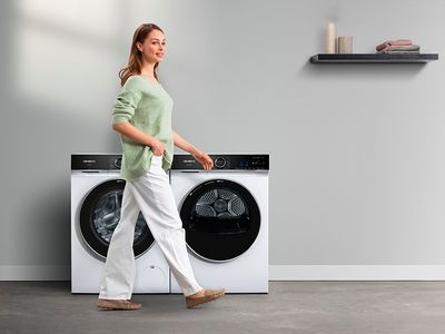 Uma lavandaria moderna com uma máquina de lavar e secar roupa branca, com uma mulher feliz a caminhar.