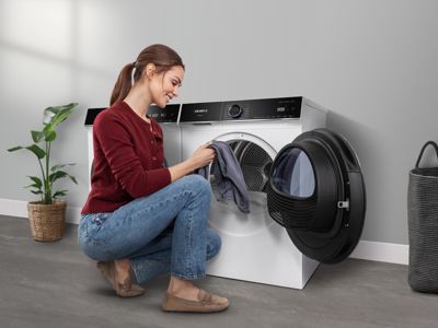 Uma pessoa segura uma camisa cinzenta amarrotada em frente a uma máquina de secar roupa com eficiência energética.