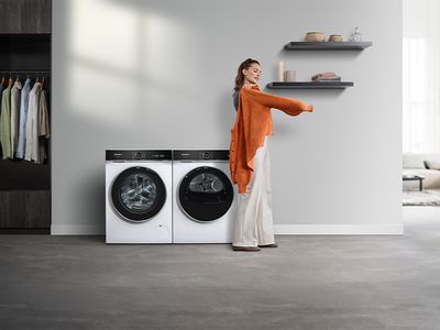 Uma mulher com uma camisola laranja ao lado de máquina de lavar e secar roupa Siemens.