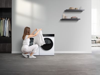 Žena v bílém oblečení vkládá bílé prádlo do pračky.