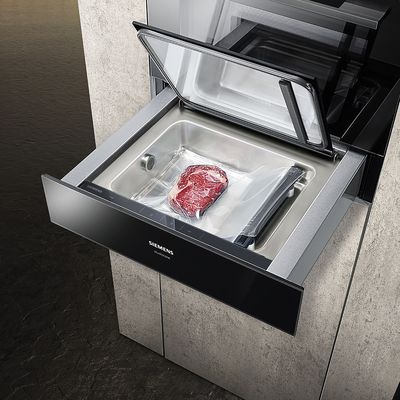 A Siemens vacuum sealer with an open drawer displaying a vacuum-packed steak, set against a sleek kitchen backdrop.